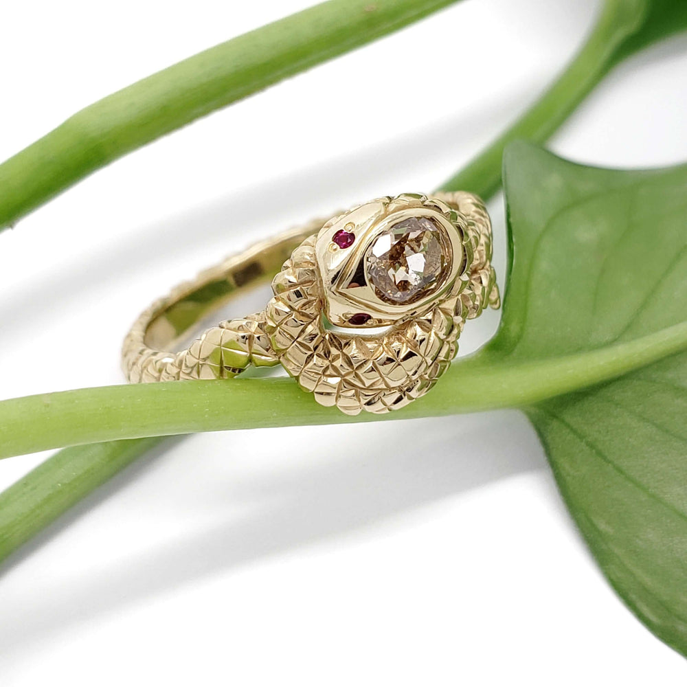Handcrafted gold snake ring with champagne diamond and rubies, shown on green leaf