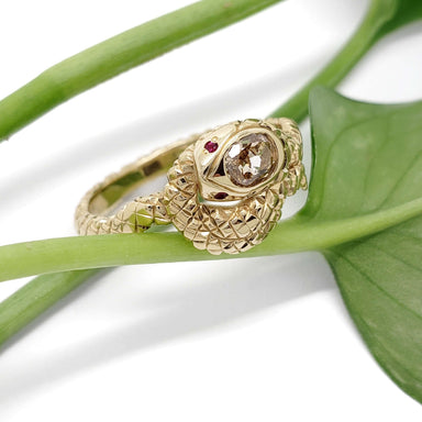 Handcrafted gold snake ring with champagne diamond and rubies, shown on green leaf
