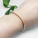 Handcrafted hammered 14kt yellow gold bangle on wrist, green leaves in background