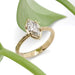 Handcrafted marquise lab diamond ring in 14kt yellow gold with engraved band, beside green leaf