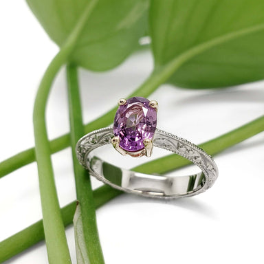 Handcrafted pink-purple sapphire ring in white and yellow gold, displayed on green leaves