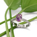 Handcrafted pink-purple sapphire ring in white and yellow gold, displayed on green leaves
