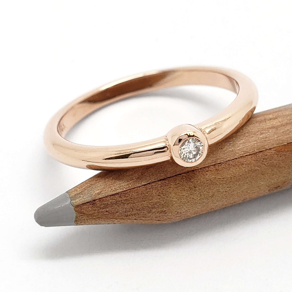 Polished rose gold ring with bezel set Canadian diamond resting on a pencil