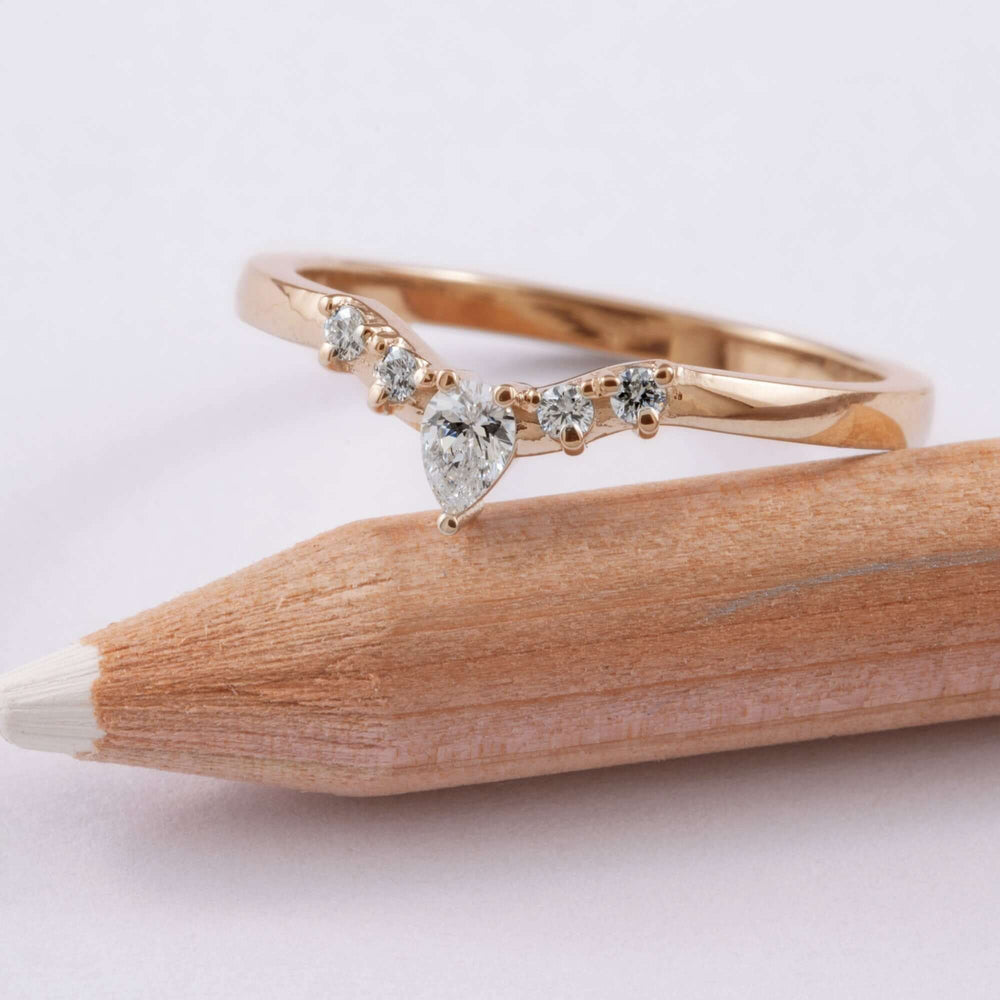 Handcrafted rose gold chevron ring with pear and round diamonds resting on a pencil