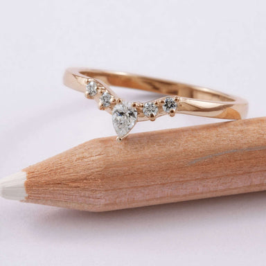 Handcrafted rose gold chevron ring with pear and round diamonds resting on a pencil