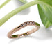 Handcrafted rose gold chevron wedding ring with diamonds beside green leaves