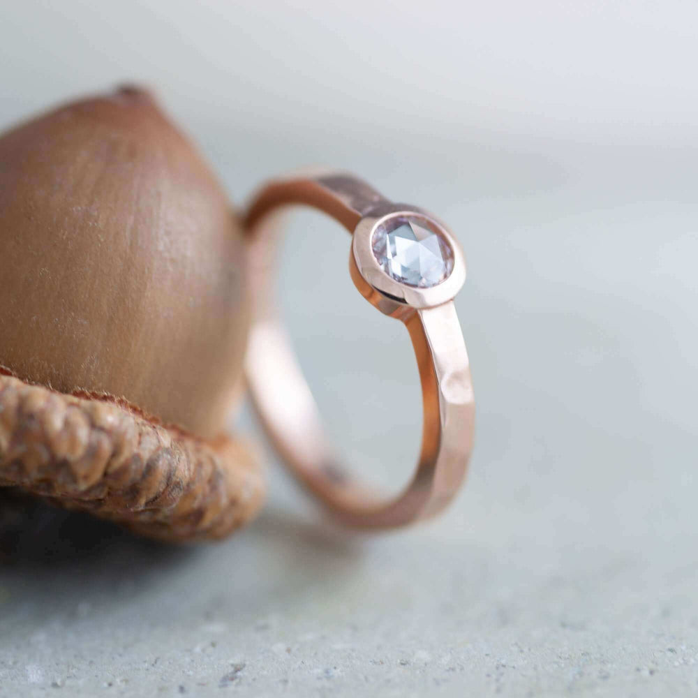 Handcrafted rose gold diamond ring with hammered band beside an acorn