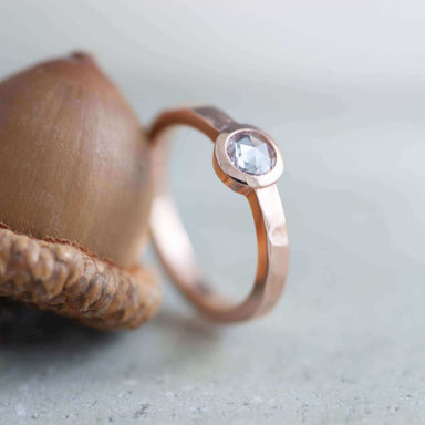 Handcrafted rose gold diamond ring with hammered band beside an acorn