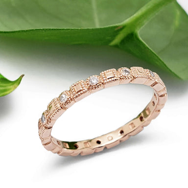 Handcrafted rose gold diamond wedding ring with millgrain detail beside green leaves