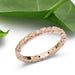 Handcrafted rose gold diamond wedding ring with millgrain detail beside green leaves