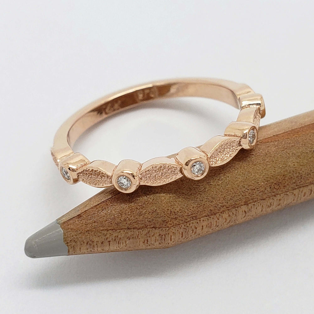 Handcrafted rose gold ring with leaf texture and bezel-set diamonds resting on a pencil