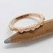 Handcrafted rose gold ring with leaf texture and bezel-set diamonds resting on a pencil