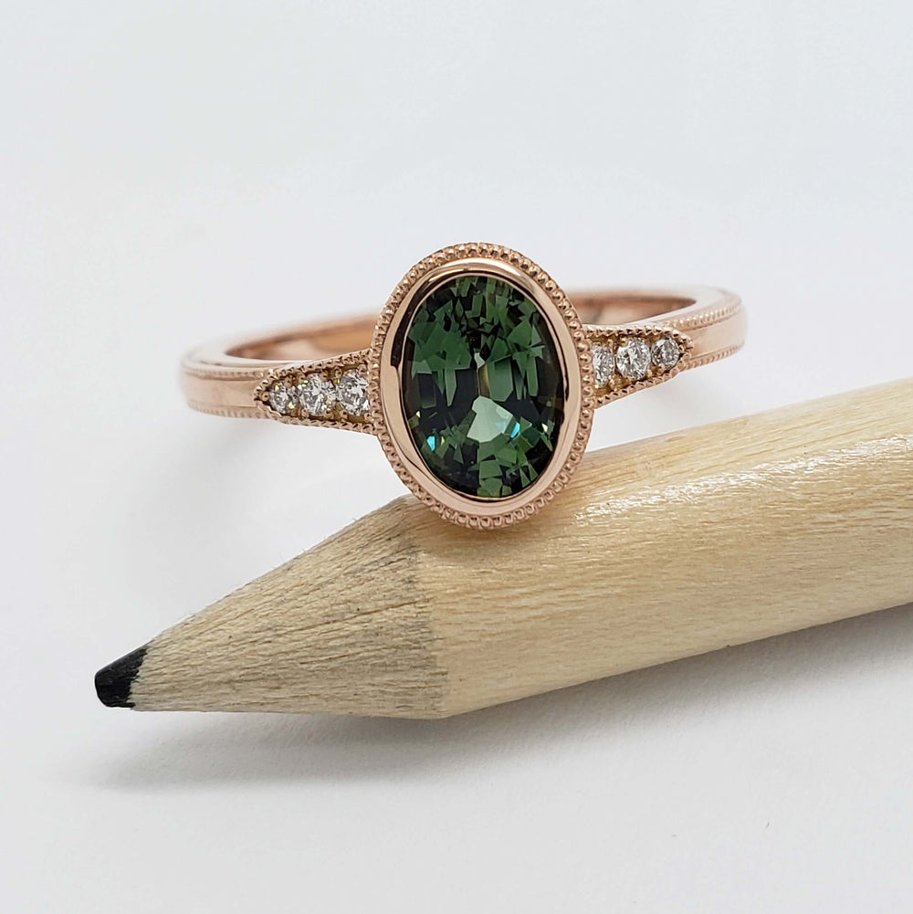 Handcrafted rose gold ring with oval green sapphire and diamond accents on a pencil