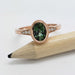 Handcrafted rose gold ring with oval green sapphire and diamond accents on a pencil