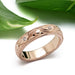 Handcrafted rose gold wedding ring with scroll engraving and diamonds, beside green leaves