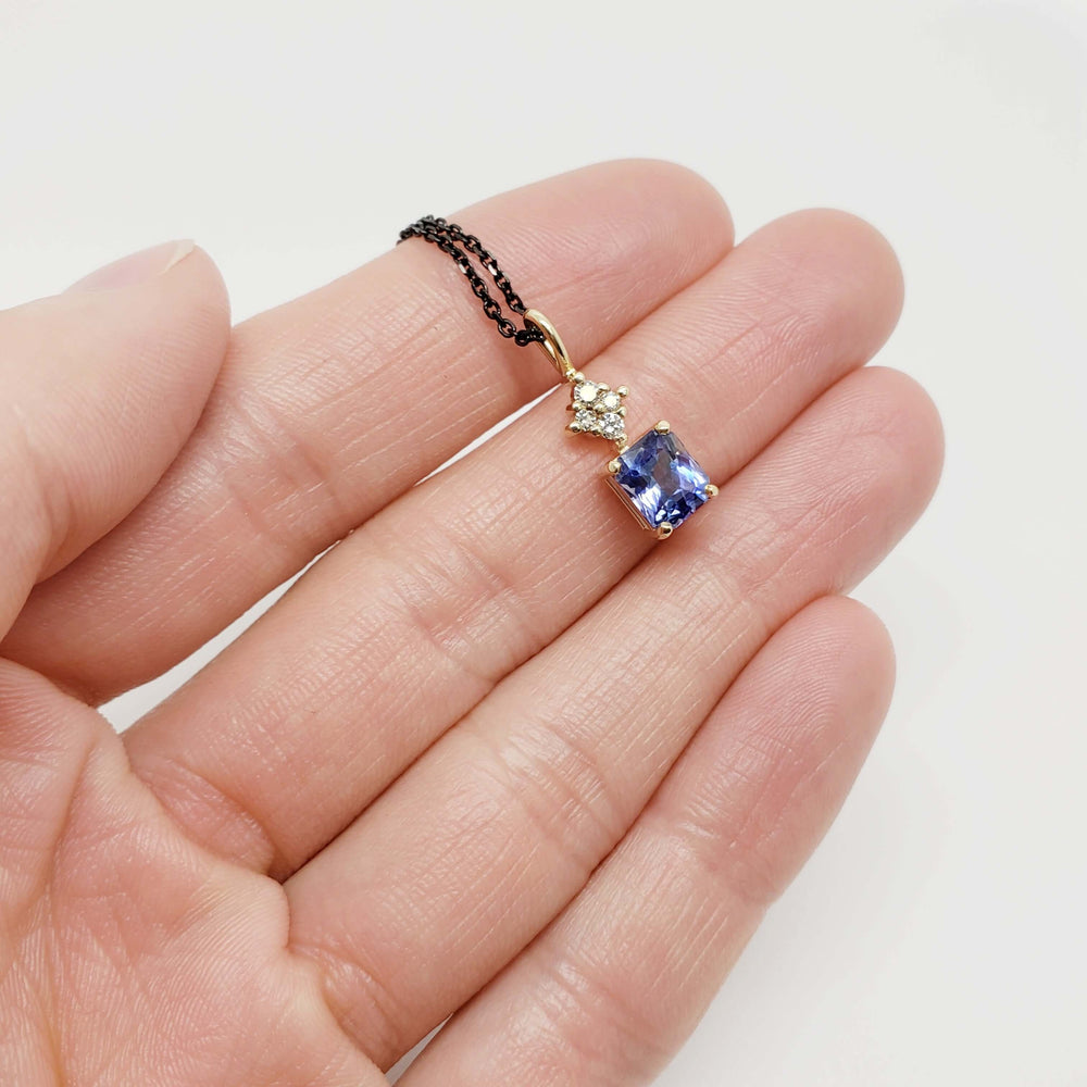 Hand holding yellow gold pendant with radiant blue sapphire and lab diamonds