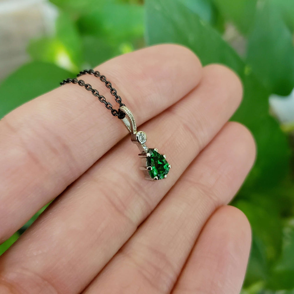 Hand holding 14kt white gold pendant with green tsavorite garnet and lab diamond