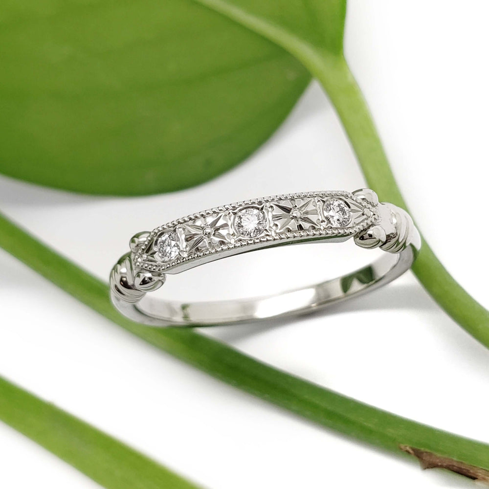 Handcrafted white gold diamond wedding ring with floral engraving, shown on a leaf background