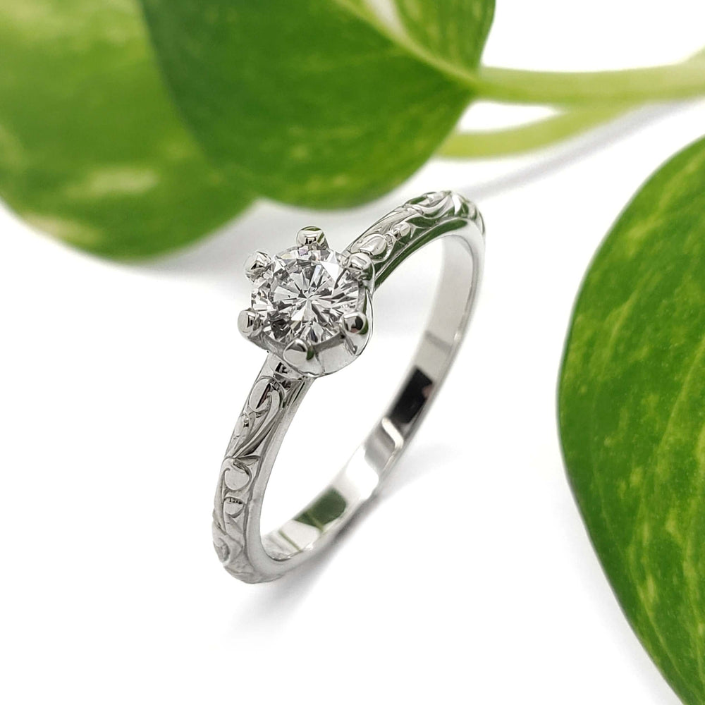 Handcrafted white gold engagement ring with antique diamond, shown with green leaves