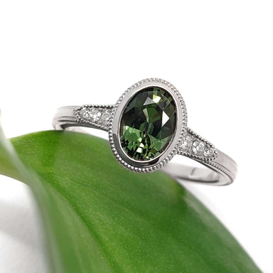 Handcrafted white gold engagement ring with oval green Australian sapphire and diamond accents on a leaf