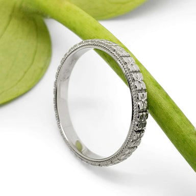 Handcrafted white gold floral wedding ring resting on a green stem