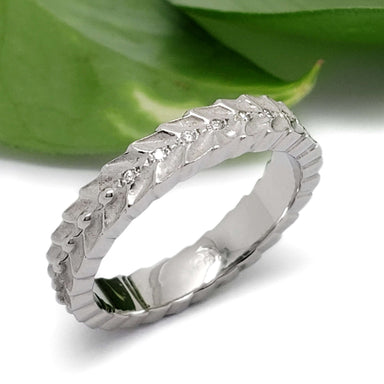 Handcrafted white gold leaf motif wedding band with diamonds, beside green leaf