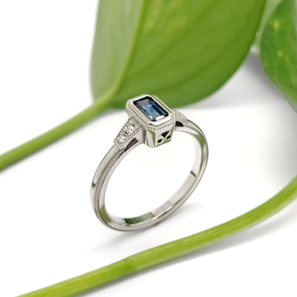 Handcrafted white gold ring with blue Montana sapphire and diamonds beside green leaves