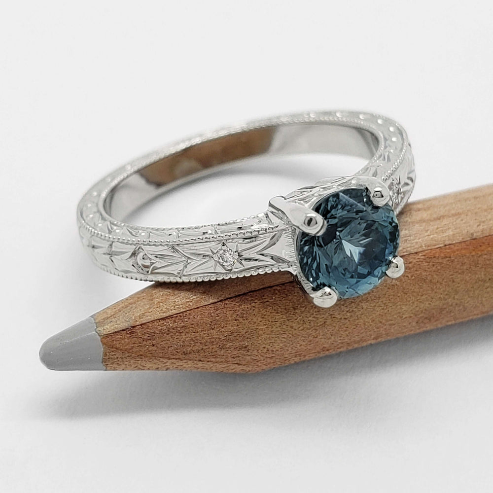 Handcrafted white gold ring with round blue Montana sapphire and diamond accents on a pencil