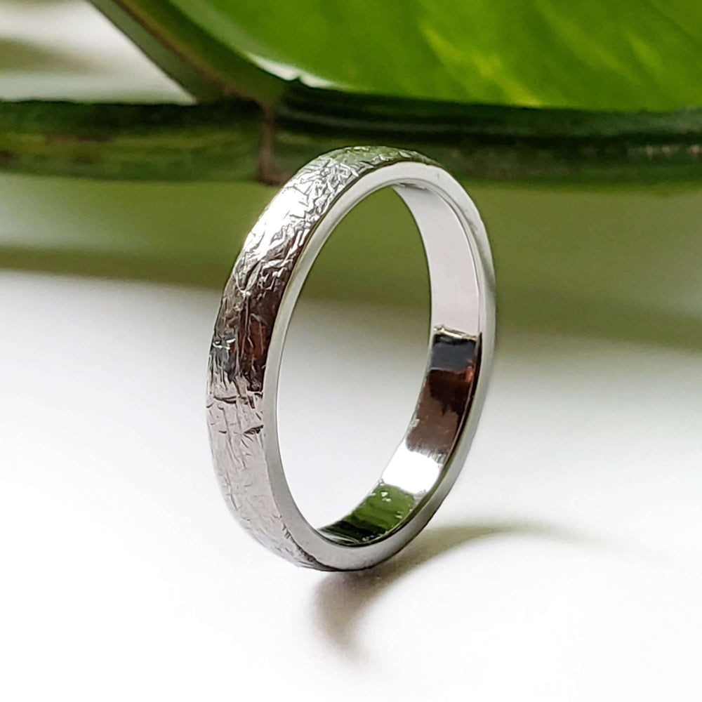 Handcrafted white gold textured wedding ring displayed with green leaf background