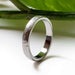 Handcrafted white gold textured wedding ring displayed with green leaf background