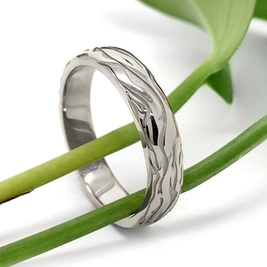 Handcrafted white gold wedding ring with bark texture, displayed on green stems