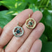 Hand holding both yellow gold and white gold circle vine sapphire pendants.