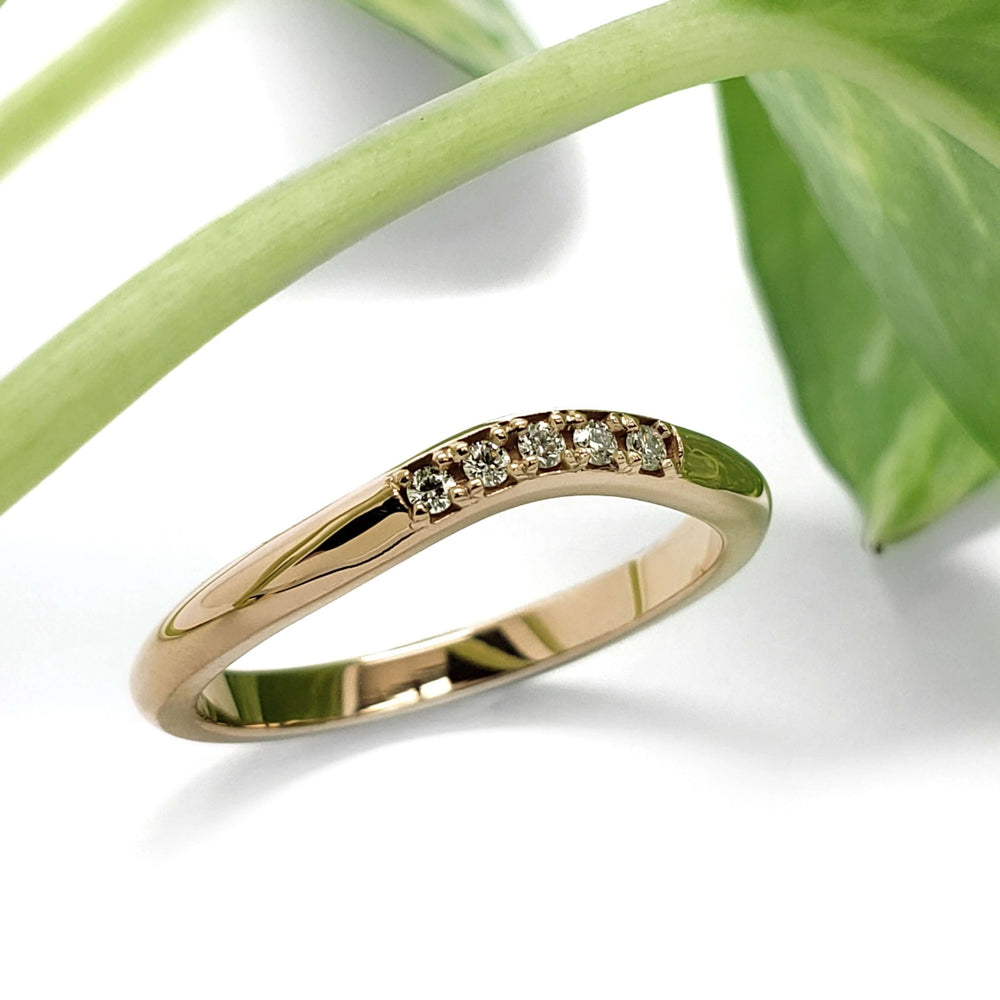 Handcrafted yellow gold chevron diamond wedding ring beside green leaves