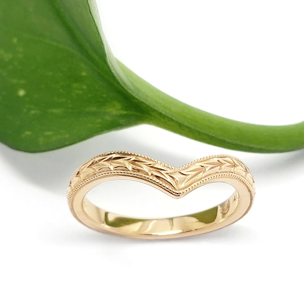 Handcrafted yellow gold chevron wedding ring with wheat engraving, shown with a green leaf
