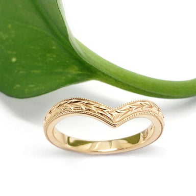 Handcrafted yellow gold chevron wedding ring with wheat engraving, shown with a green leaf