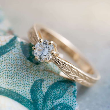 Handcrafted yellow gold diamond engagement ring with wheat engraved band on patterned background