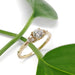 Handcrafted yellow gold diamond ring displayed with green leaves