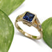 Handcrafted yellow gold engagement ring with blue sapphire and diamond accents, shown with leaves