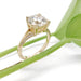 Handcrafted yellow gold engagement ring with round lab diamond and pave band beside green leaf