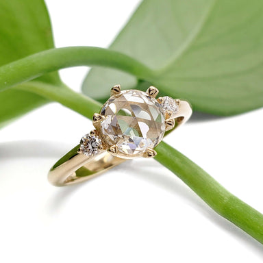 Handcrafted yellow gold lab diamond ring with rose cut center stone, shown with green leaves