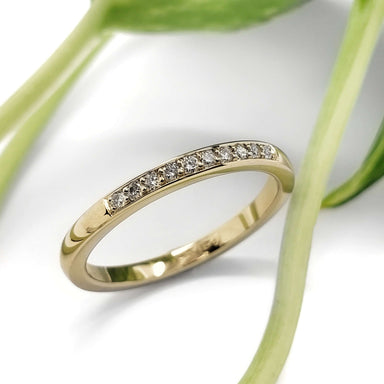 Handcrafted yellow gold lab diamond wedding band with pave setting, beside green leaves