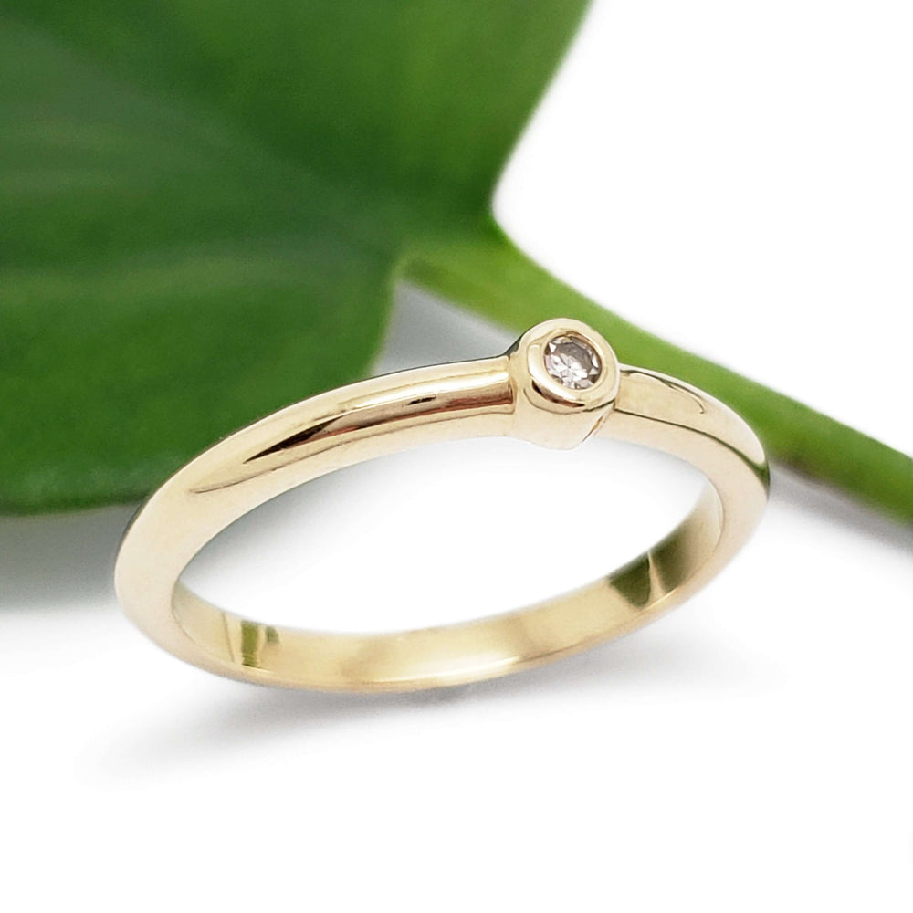 Handcrafted yellow gold ring with bezel set diamond beside a green leaf