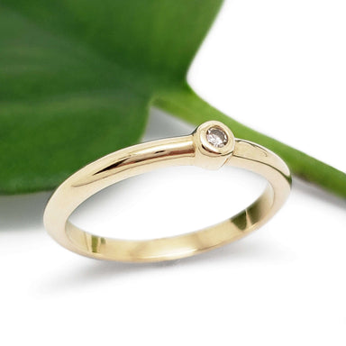 Handcrafted yellow gold ring with bezel set diamond beside a green leaf