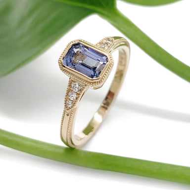 Handcrafted yellow gold ring with blue sapphire and diamonds, shown with green leaf