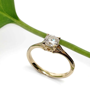 Handcrafted yellow gold ring with cushion lab diamond beside a green leaf