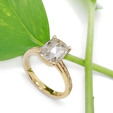 Handcrafted yellow gold ring with cushion rose cut lab diamond beside a green leaf