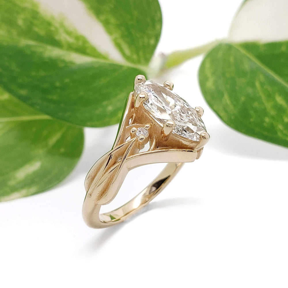 Handcrafted yellow gold ring with moval lab diamond and side stones, shown with green leaves