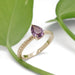 Handcrafted yellow gold ring with pink sapphire, engraved band, beside green leaves