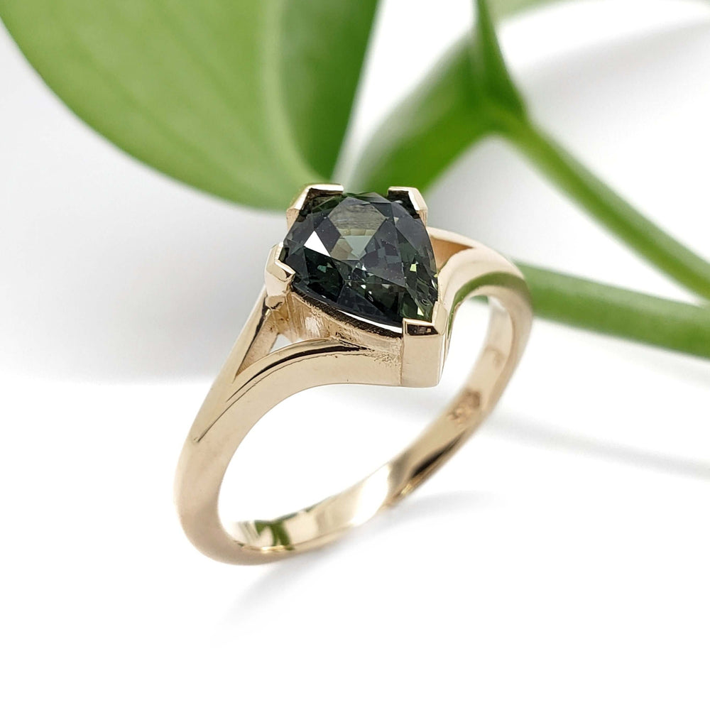Handcrafted yellow gold ring with teal sapphire, split-shank design, near green leaf