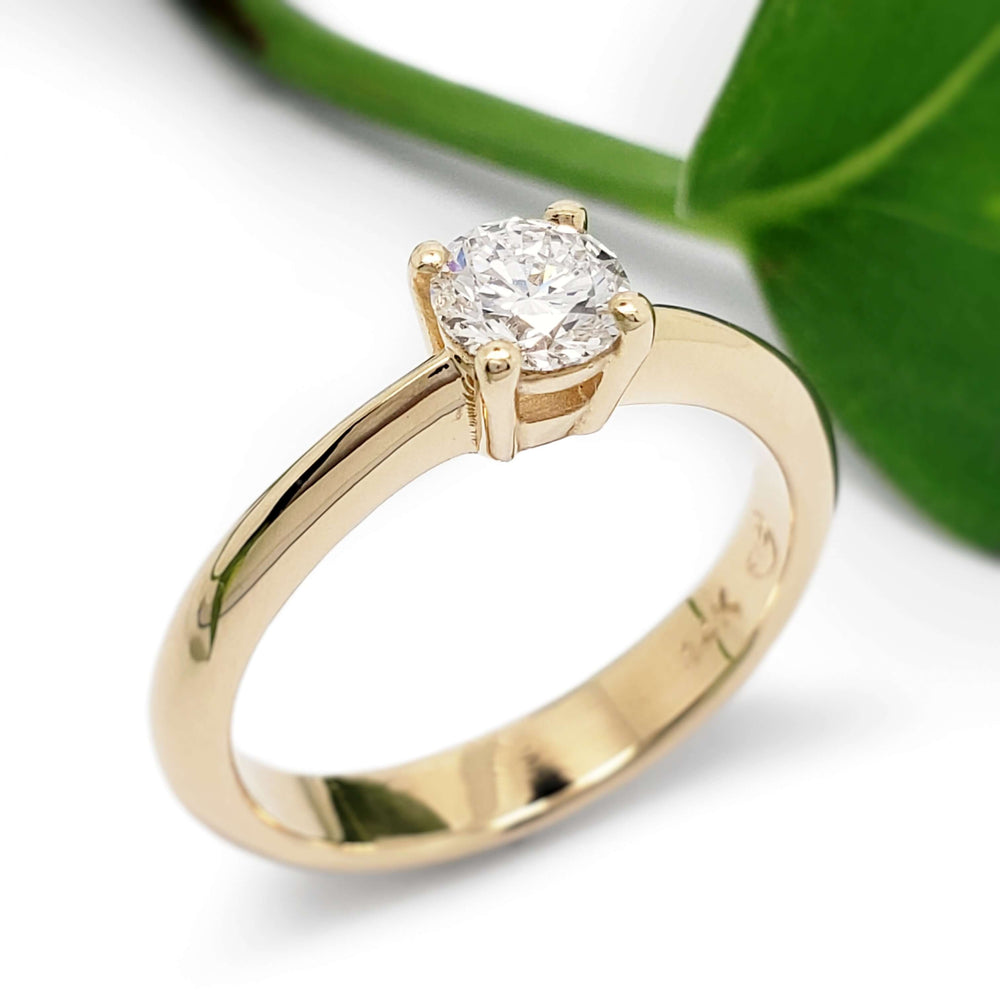Handcrafted yellow gold solitaire ring with round brilliant diamond, near green leaf